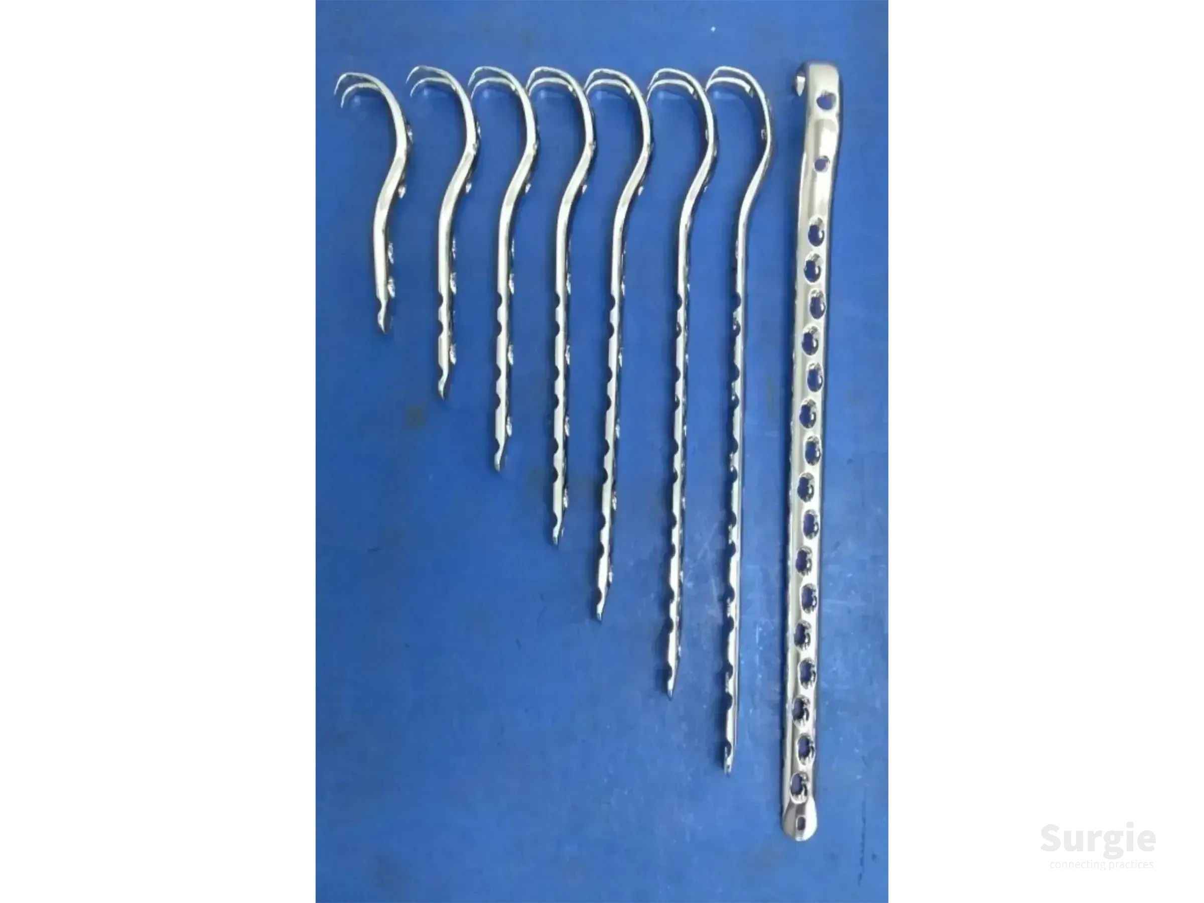 Set of metallic surgical trochanteric plates and a long fixation plate on a blue background.